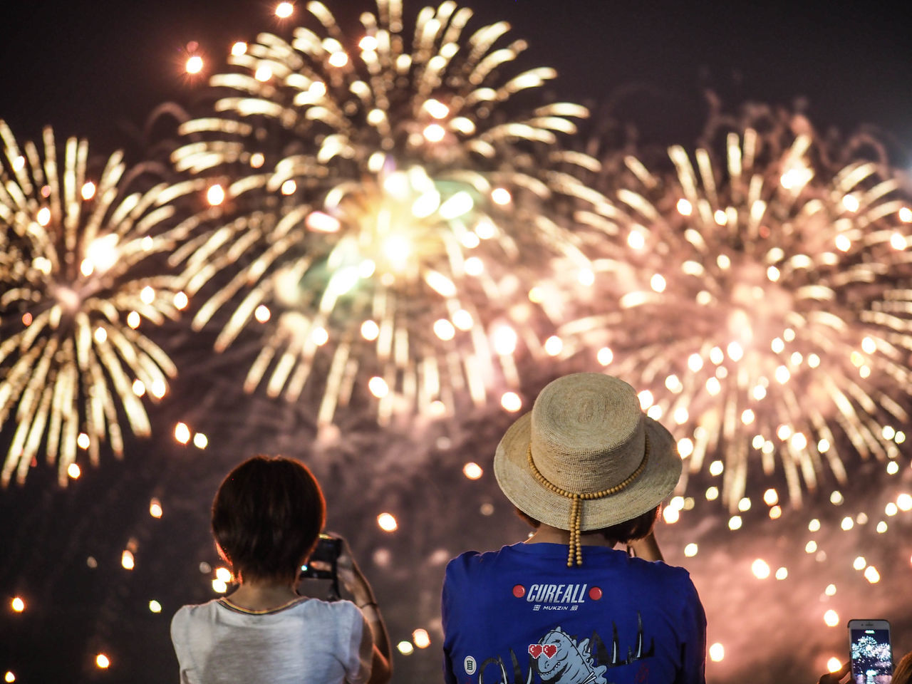 REAR VIEW OF WOMAN STANDING AGAINST ILLUMINATED FIREWORK DISPLAY