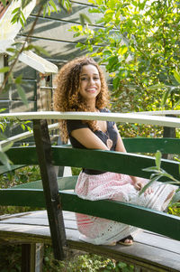 Portrait of smiling young woman crouching on footbridge at park