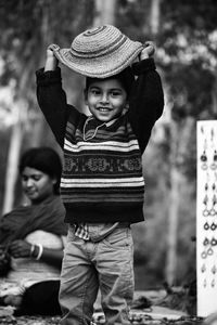 Portrait of smiling boy wearing hat while standing against mother in park