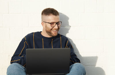 Young man using mobile phone while sitting on wall