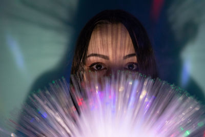 Close-up portrait of young woman holding multi colored fiber optic
