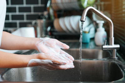 Close-up of hand touching water from faucet at home