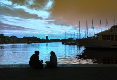 Silhouette of people sitting on riverbank