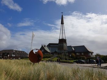 Traditional windmill on field by buildings against sky