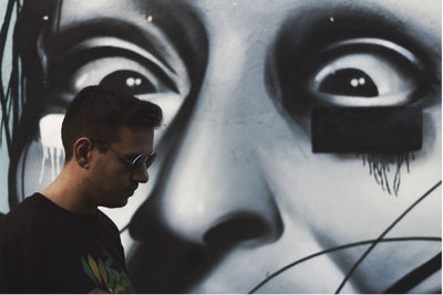 Young man wearing sunglasses by graffiti wall