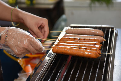 Cropped hand of person preparing sausages on barbecue grill