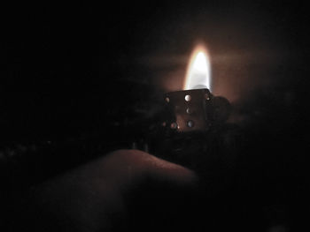 Close-up of hand holding lit candle in the dark