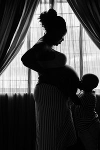 Side view of boy kissing pregnant mother belly at home