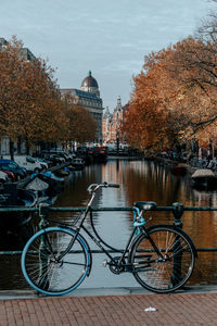 Bicycle by river in city against sky