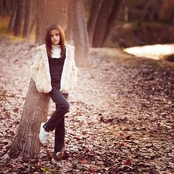 Full length portrait of girl leaning on tree at field