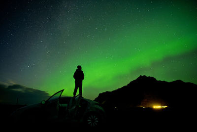 Silhouette man standing on car roof against aurora borealis