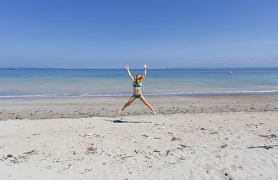 Full length of woman in bikini jumping at beach against clear blue sky