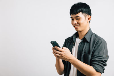 Young man using mobile phone while standing against white background
