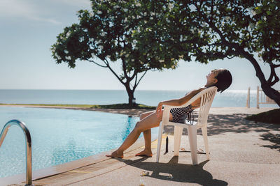 Woman having sunbathing by swimming pool outdoors at summer time.