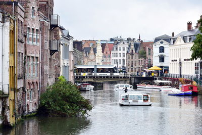 Boats in river by buildings in city against sky