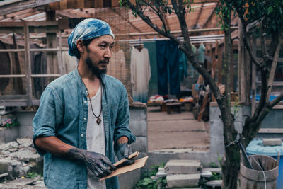 Man looking away while standing against shed