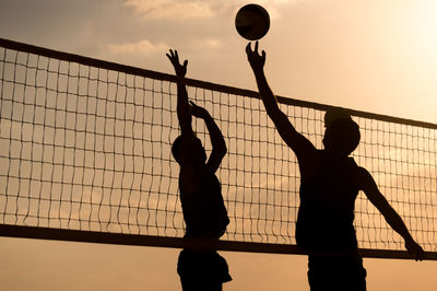 Silhouette men playing volleyball against sky during sunset