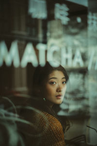Portrait of young woman sitting in cafe seen through window