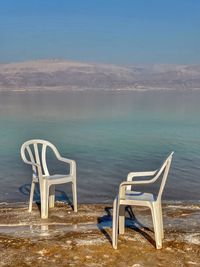 Chair on shore by sea against sky