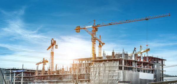 Low angle view of cranes at construction site against sky