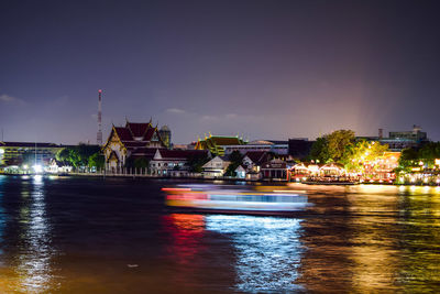 Illuminated buildings by river against sky in city at night