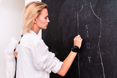 Side view of fashion designer drawing on blackboard