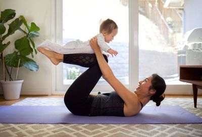 Side view of happy woman playing with baby while exercising at home