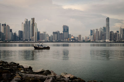 Boats in sea by buildings against sky in city