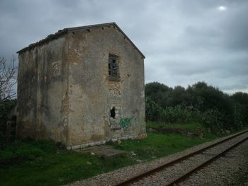Old abandoned building by railroad tracks against sky