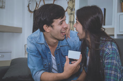 Young man with girlfriend holding business card while sitting on sofa at home