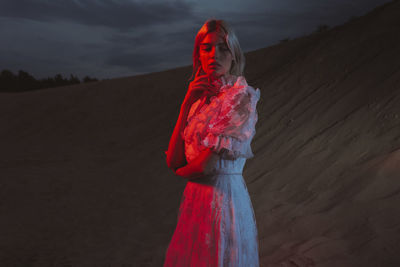 Woman in a long dress standing near a sandy hill in the evening