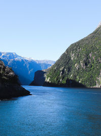 Scenic view of sea and mountains against clear blue sky