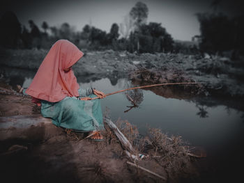 Woman holding umbrella by lake against sky