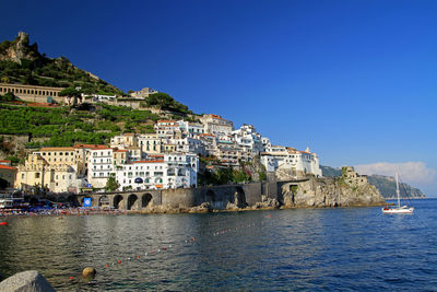 Buildings by sea against clear blue sky