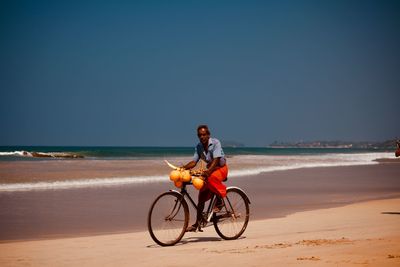 Man riding bicycle on beach against clear sky