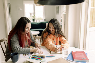 Happy woman assisting daughter in homework while sitting at table