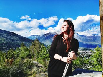 Smiling woman holding hiking poles while standing on mountain against sky