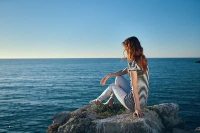 Full length of woman sitting on rock against sea