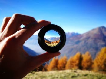 Mountains seen through lens being held by person