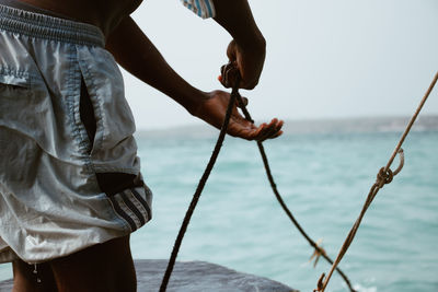 Midsection of man holding umbrella by sea against sky