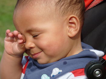 Close-up of cute smiling boy rubbing eyes