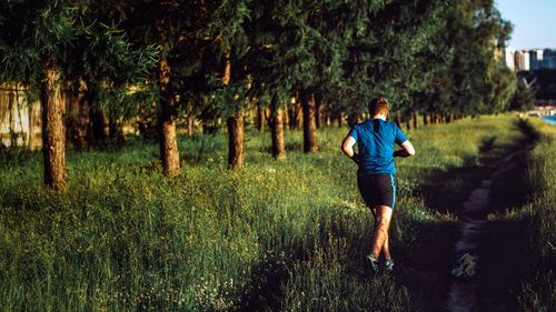 Rear view of young man running on grassy field in park