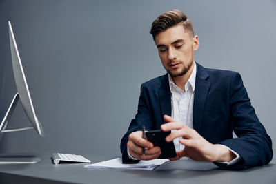 Young man using mobile phone while standing against wall