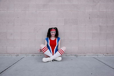 Young woman in sports clothing sitting against wall