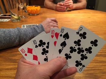 Cropped hand holding playing cards at table at home