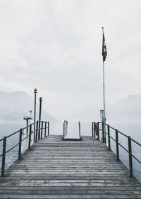 Swiss flag on pier over lake against cloudy sky