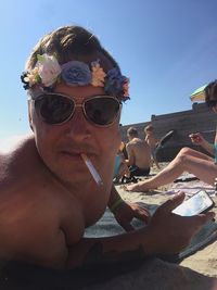 Portrait of man smoking while lying on sand at beach against clear sky