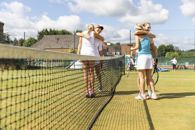 Mature women finishing tennis match on grass court hugging