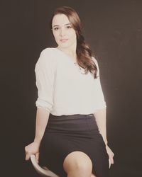 Portrait of young woman standing against black background