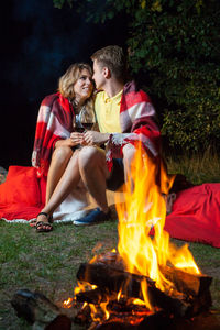 Young couple sitting on bonfire against trees